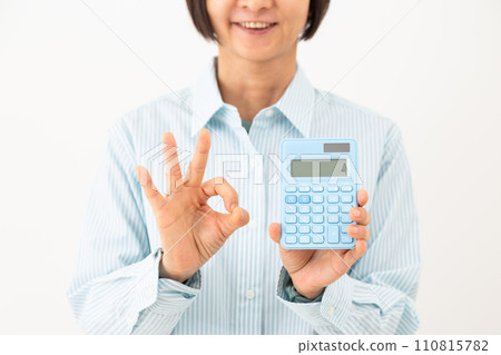 A middle-aged woman holding a blue calculator and making a circle sign 110815782