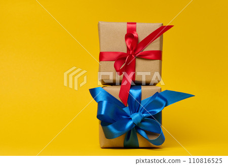 Box is wrapped in brown paper and ribbon on a yellow background. Box is wrapped in brown paper and ribbon on a yellow background. 110816525