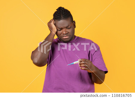 Sick black guy measuring temperature looking at thermometer, yellow background 110816705