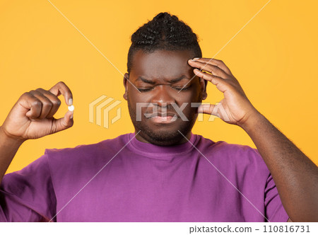 African american man having painful headache holding painkiller pill, studio African american man having painful headache holding painkiller pill, studio 110816731