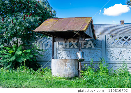 Old well with iron bucket on long forged chain for clean drinking water 110816792