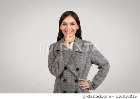 Smiling woman in a blazer gesturing silence 110816819