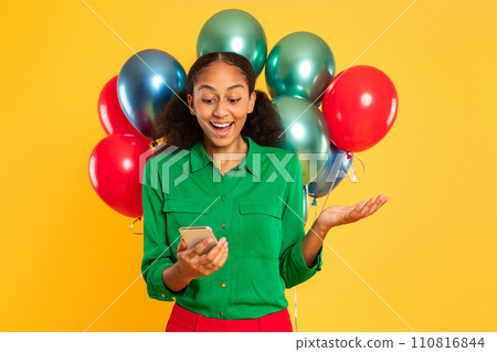 Excited African teenager girl texting on phone with balloons, studio Excited African teenager girl texting on phone with balloons, studio 110816844