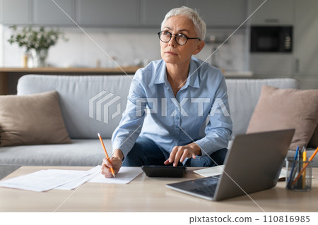 senior woman sitting with laptop and taking notes at home 110816985