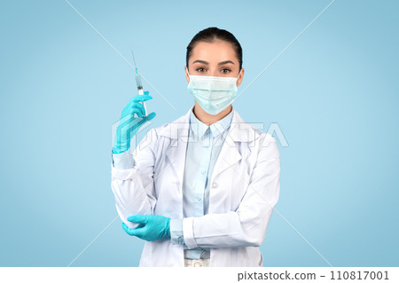 European lady doctor in white coat and surgical mask holding syringe, preparing for vaccination or medical procedure European lady doctor in white coat and surgical mask holding syringe, preparing for vaccination or medical procedure 110817001