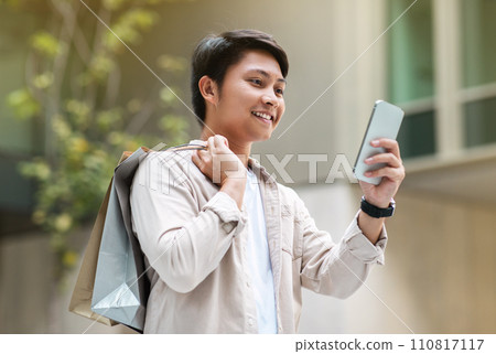 Cheerful chinese man shopping at city center, using smartphone Cheerful chinese man shopping at city center, using smartphone 110817117