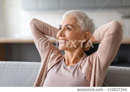 mature woman leaning back on sofa holding hands behind head 110817164