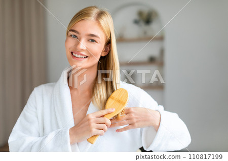 Blonde lady enjoying self pampering brushing long straight hair indoors Blonde lady enjoying self pampering brushing long straight hair indoors 110817199