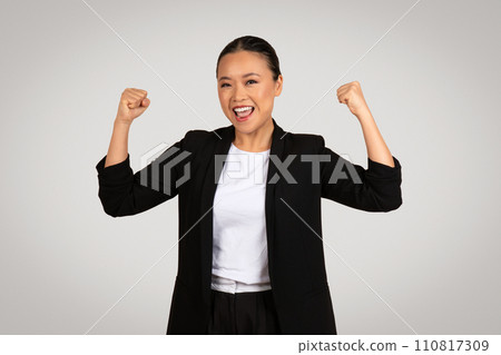 Exuberant Asian businesswoman in a smart black suit with fists pumped in the air 110817309