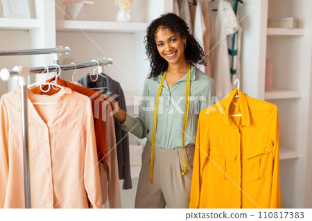 Smiling fashion designer with clothes on rack 110817383