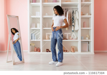 Contemplative woman in loose jeans, considering weight loss Contemplative woman in loose jeans, considering weight loss 110817384