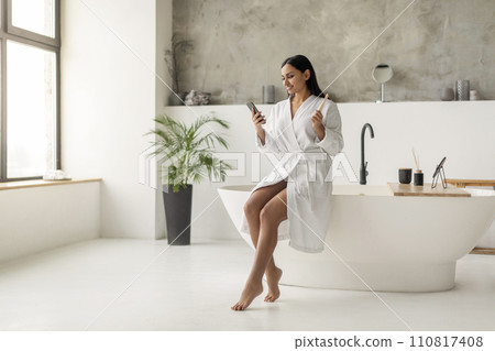 Smiling young indian woman using smartphone after shower Smiling young indian woman using smartphone after shower 110817408
