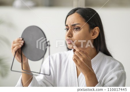 Unhappy eastern young woman in white robe looking at mirror 110817445