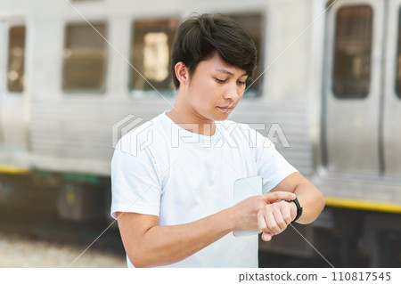 Asian guy looking at watch standing on city street Asian guy looking at watch standing on city street 110817545