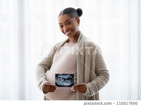 Cheerful young pregnant african american woman showing baby sonogram Cheerful young pregnant african american woman showing baby sonogram 110817600