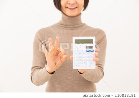 A middle-aged woman holding a white calculator and making a circle sign A middle-aged woman holding a white calculator and making a circle sign 110818181