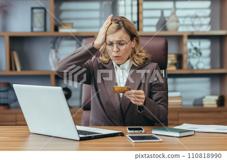 Mature businesswoman experiences stress handling personal finances or work expenses, looking at credit card with concern. 110818990