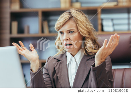 An exasperated mature female executive experiences trouble while working from her stylish home office setting. 110819038