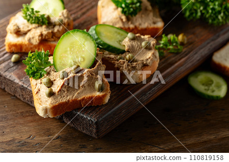 Open sandwiches with pate, cucumber, capers, and parsley on a old cutting board. Open sandwiches with pate, cucumber, capers, and parsley on a old cutting board. 110819158