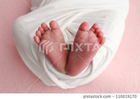 The tiny foot of a newborn baby. Soft feet of a new born in a white blanket. Close up of toes, heels and feet of a newborn. Macro photography on the pink background 110819170