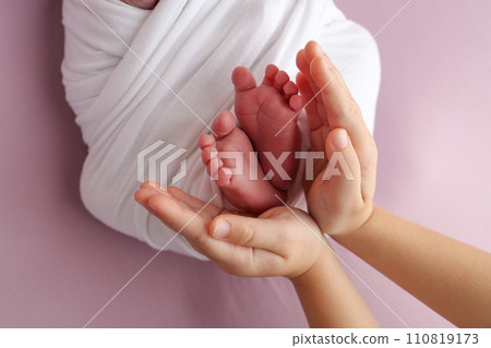The palms of the father, the mother are holding the foot of the newborn baby in a white blanket, pink background. Feet of the newborn on the palms of the parents. photo child's toes, heels and feet. The palms of the father, the mother are holding the foot of the newborn baby in a white blanket, pink background. Feet of the newborn on the palms of the parents. photo child's toes, heels and feet. 110819173