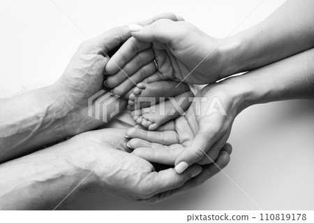 The palms of the father, the mother are holding the foot of the newborn baby. Feet of the newborn on the palms of the parents. Studio macro black and white photo of a child's toes, heels and feet. The palms of the father, the mother are holding the foot of the newborn baby. Feet of the newborn on the palms of the parents. Studio macro black and white photo of a child's toes, heels and feet. 110819178