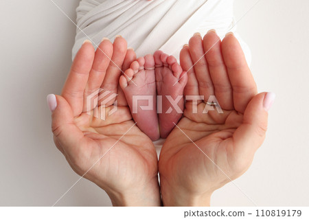 The palms of the father, the mother are holding the foot of the newborn baby in a white blanket. Feet of the newborn on the palms of the parents. Studio macro photo of a child's toes, heels and feet. 110819179