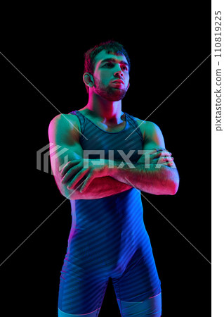 Young athlete man, Greco-Roman fighter in sportwear posing against black background in mixed neon lights. Colored gel portraits 110819225