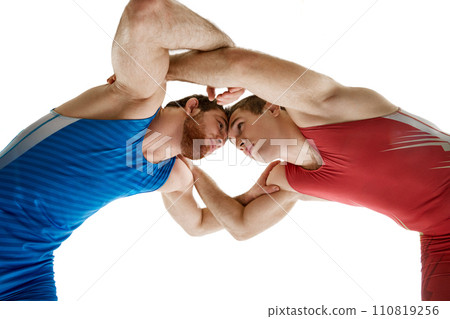 Two young, skilled and professional freestyle wrestlers in red and blue fighting uniform against white studio background. Two young, skilled and professional freestyle wrestlers in red and blue fighting uniform against white studio background. 110819256