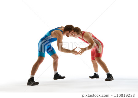 Young athlete man, wrestlers in blue and red uniform hand wrestling in neutral position on their feet against white studio background. 110819258
