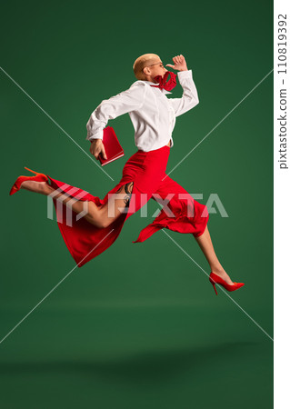Hurry up. Dynamic side view portrait of business lady in trendy office wear running to work in mid-air against green studio background. Hurry up. Dynamic side view portrait of business lady in trendy office wear running to work in mid-air against green studio background. 110819392