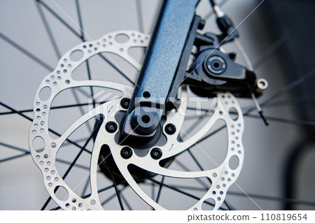 Part of the bicycle's braking system. Grey metal brake disc and brake pads on road bike, close up. Part of the bicycle's braking system. Grey metal brake disc and brake pads on road bike, close up. 110819654