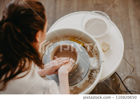 Forming the walls of a clay product on a potter's wheel. Pottery, female hands of a potter create a product from white clay. Top view 110820650