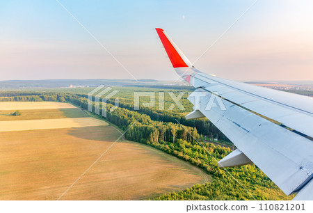 View of airplane wing, blue skies and green land during landing. Airplane window view. View of airplane wing, blue skies and green land during landing. Airplane window view. 110821201