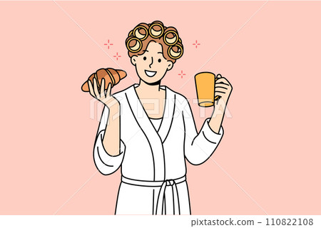 Woman enjoys morning breakfast of fresh croissant and cup coffee, standing in bathrobe and curlers Woman enjoys morning breakfast of fresh croissant and cup coffee, standing in bathrobe and curlers 110822108