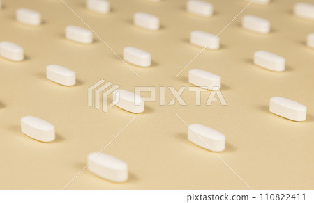 Close-up of a pattern of white pills on a beige background. 110822411