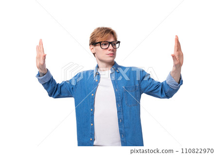 a young positive red-haired guy dressed in a blue shirt gesticulates with his hands a young positive red-haired guy dressed in a blue shirt gesticulates with his hands 110822970