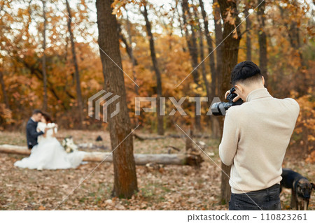 Professional wedding photographer taking pictures of the bride and groom in nature in autumn Professional wedding photographer taking pictures of the bride and groom in nature in autumn 110823261
