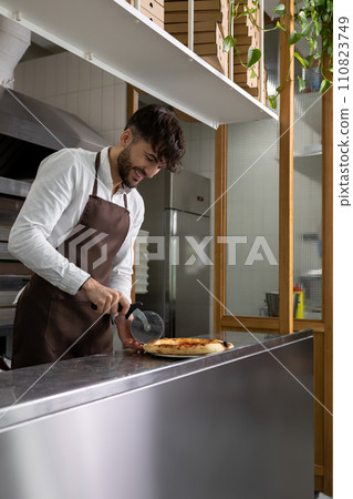 Dark-haired young man cooking pizza in pizzeria Dark-haired young man cooking pizza in pizzeria 110823749
