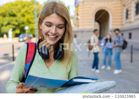 University female student standing with book in hands reading with smiling face. University female student standing with book in hands reading with smiling face. 110823965