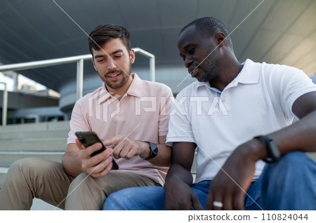 Two colleagues sitting together on steps and talking 110824044