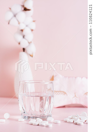 Sleeping pills, a glass of water and a sleep mask on a pink background vertical view Sleeping pills, a glass of water and a sleep mask on a pink background vertical view 110824121
