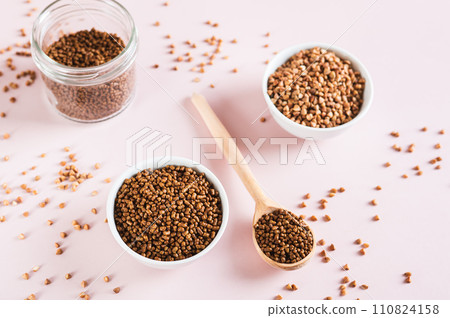 Raw buckwheat tea in a bowl and wooden spoon and buckwheat on the table 110824158