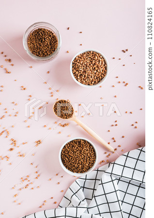 Raw buckwheat tea in a bowl and wooden spoon and buckwheat on the table top and vertical view 110824165