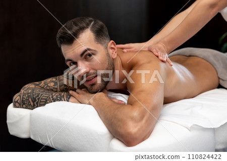 Young man with a big tattoo having back massage session in a salon Young man with a big tattoo having back massage session in a salon 110824422