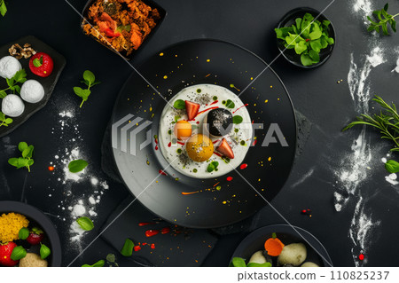 Plate with dessert on a dark table, ingredients laid out nearby, vegetarian molecular cuisine food concept 110825237