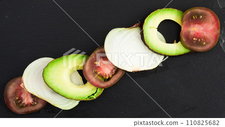 chopped vegetables black tomatoes, avocado and onions against black stone board 110825682