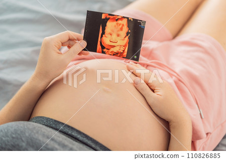 Expectant mother tenderly connects with her unborn child, holding ultrasound photo to her pregnant belly Expectant mother tenderly connects with her unborn child, holding ultrasound photo to her pregnant belly 110826885