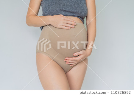 Pregnant bliss: Mom-to-be embraces her baby bump with a soft fabric bandage, providing gentle support. Maternity made comfortable 110826892