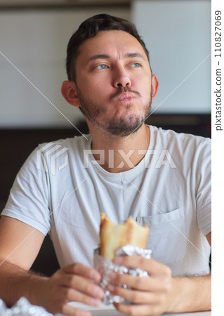 Closeup portrait of hungry man eating delicious sandwich at home on background of kitchen. Handsome male enjoying vegetarian dinner indoors. Caucasian guy eating toast in morning, slow motion. Closeup portrait of hungry man eating delicious sandwich at home on background of kitchen. Handsome male enjoying vegetarian dinner indoors. Caucasian guy eating toast in morning, slow motion. 110827069
